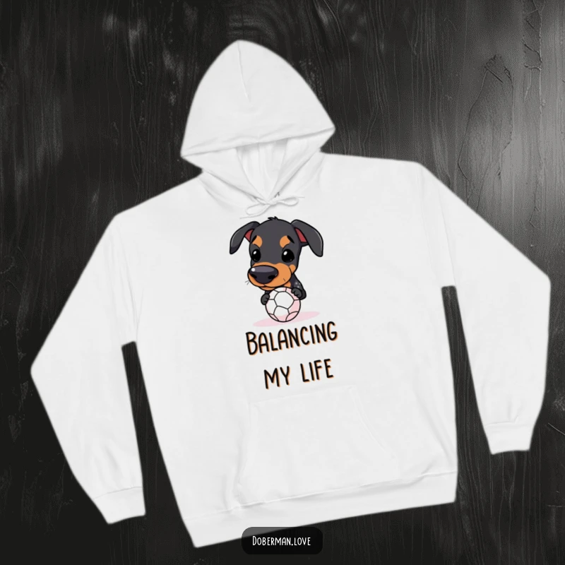 Funny Kawaii Doberman Hoodie featuring a dog trying to balance a ball on its snout, for cozy humor.